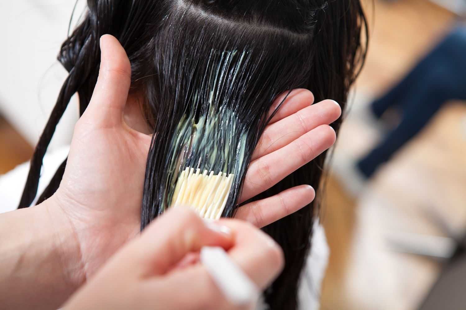 Close-up of a hairdresser applying hair dye to client's hair with a brush.