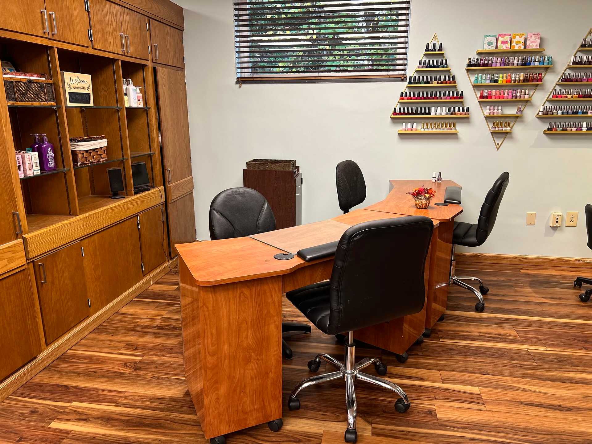 Nail salon interior with wooden furniture, nail polish displays on walls, and manicure stations.
